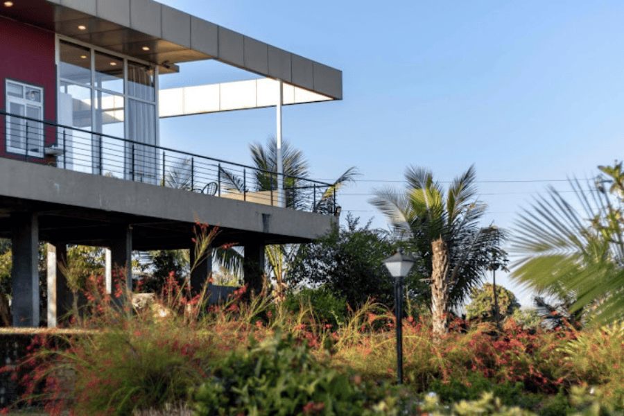 Modern villa in Nashik with lush garden, balcony seating, and tropical views under clear sky.