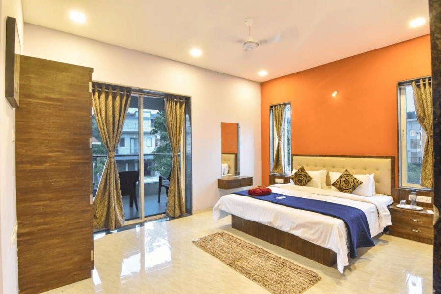 Luxurious bedroom with king bed, balcony, and orange wall for Lonavala luxury stay.
