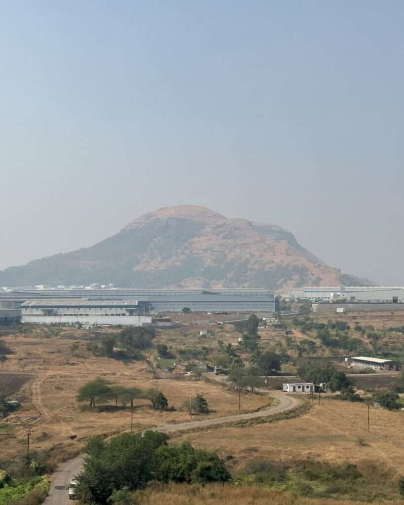 Hill stands beyond sunlit fields and scattered homes under a soft, hazy sky.