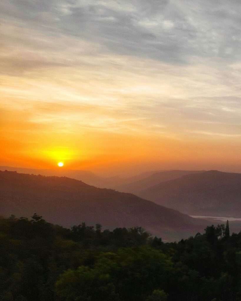Golden sunrise over misty mountain layers and forested valleys under a cloudy sky.