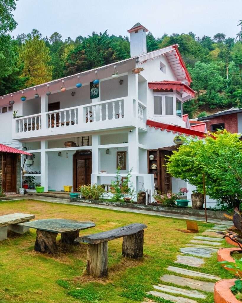 Charming white villa in Mukteshwar with garden seating and scenic forest backdrop.